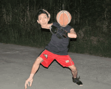 a man in a black shirt and red shorts holds a basketball in front of his face