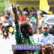 a woman wearing a mask holds her hand up in front of a crowd with the words lanjutkan on the bottom