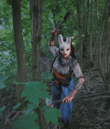 a woman in a dead by daylight costume is holding a bloody axe in the woods .