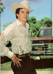 a man wearing a cowboy hat and striped shirt is standing in front of a truck