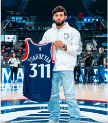 a man holds up a basketball jersey that says tsarukyan 311