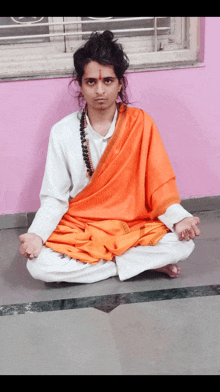 a man in an orange robe sits in a lotus position on the floor