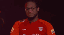 a man wearing glasses and a red nike shirt is smiling in a dark room .