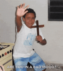 a young boy is holding a wooden cross and waving at the camera with the words are you in a bad mood below him