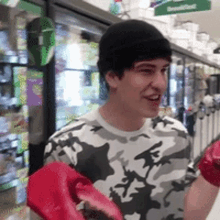 a man in a camo shirt is holding a pair of red gloves