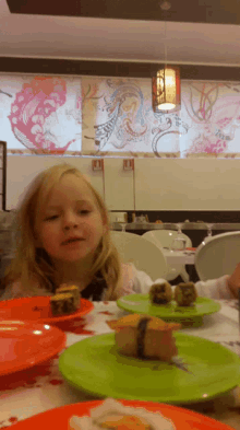 a little girl sits at a table with plates of food in front of a sign that says ' no smoking '