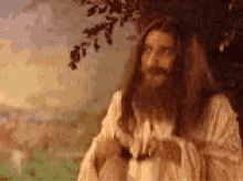 jesus with long hair and a beard is standing in front of a tree .