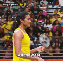 a woman in a yellow tank top is holding a badminton racket in front of a crowd and says `` all the best ''