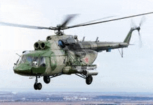 a green military helicopter is flying in the sky over a field .