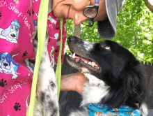 a man kisses a black and white dog wearing a shirt that says sit stay hear