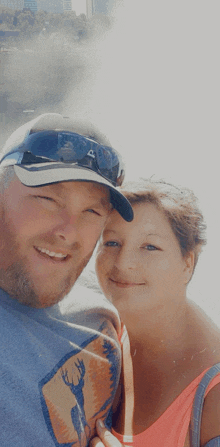 a man and a woman are posing for a picture and the man is wearing a hat