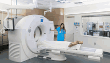 a woman in a blue scrub is standing next to a siemens machine