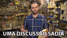 a man in a plaid shirt is holding a book in front of a wall of tools and the words uma discussao sadia above him