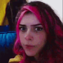 a girl with pink hair is eating a banana and making a face .