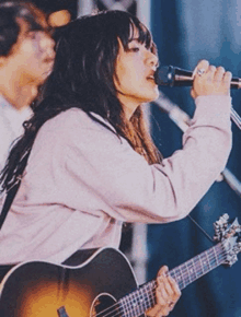 a woman sings into a microphone while playing a guitar