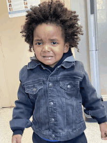 a little boy in a denim jacket is crying in front of a wall with pictures of children on it