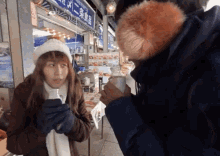 a woman in a white hat holds a cup in front of a store with chinese writing on the sign