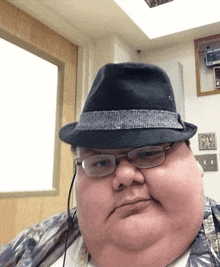 a fat man wearing glasses and a fedora looks at the camera