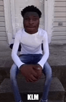 a young man in a white shirt and blue jeans is sitting on steps .