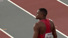 a man in a red and blue striped tank top with coleman on the back is standing on a track .