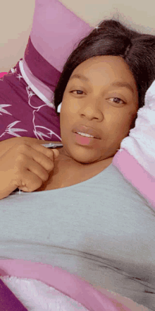 a woman in a grey shirt is laying on a bed with purple pillows