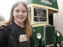 a girl wearing a billie eilish shirt smiles in front of a canterbury double decker bus