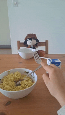 a person is eating noodles with a fork and spoon while a stuffed animal sits on a chair in the background