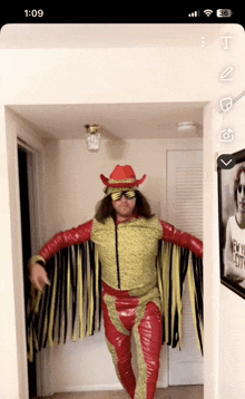 a man in a cowboy costume is standing in a hallway with a picture of john lennon on the wall