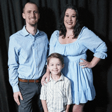 a woman in a blue dress stands next to a man and boy