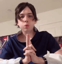 a young boy in a blue shirt is praying with his hands folded