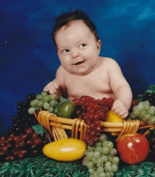 a baby is sitting in a basket filled with fruit and vegetables .