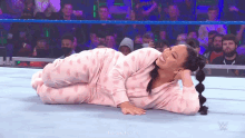 a woman in pink pajamas is laying on the ground in a wrestling ring .