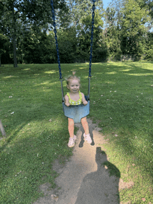 a little girl is sitting on a blue swing in a park