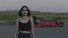 a woman is standing in front of a red car that has turned over .