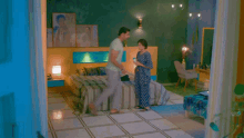 a man in a blue shirt is holding a woman in a bedroom