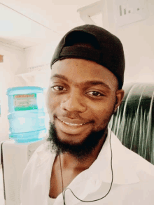 a man wearing a black hat and a white shirt is smiling in front of a water cooler that says drinkingwater on it