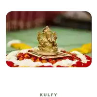 a statue of ganesha sits on a table with flowers and the word kulfy below it