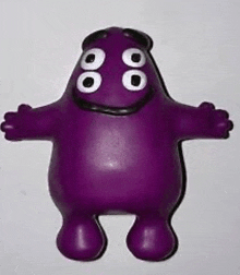 a purple toy with white eyes and black hair is sitting on a white surface .