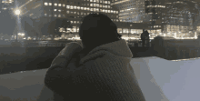 a person in a sweater stands in front of a city skyline at night