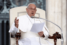 a man in a white robe is sitting in a chair speaking into a microphone