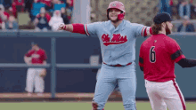 a baseball player wearing a blue ole miss jersey stands next to another player wearing a red jersey with the number 6 on it