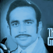 a man with a mustache is holding a microphone with the letters tg behind him