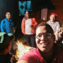 a group of men are posing for a selfie in front of a fire pit .