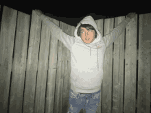 a person wearing a grey nike hoodie is standing in front of a wooden fence with their arms outstretched