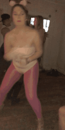 a woman in pink leggings and bunny ears is dancing in a room