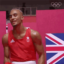 a man in a red tank top is standing in front of a pink wall with a british flag .