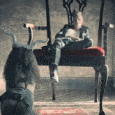 a woman with horns is kneeling down in front of a man sitting in a chair