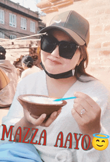 a woman wearing sunglasses and a hat is holding a bowl of food with the words mazza aayo on the bottom