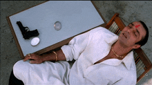 a man in a white shirt is laying on a chair next to a gun