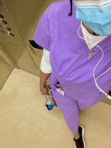 a nurse wearing purple scrubs and a mask stands in front of an elevator